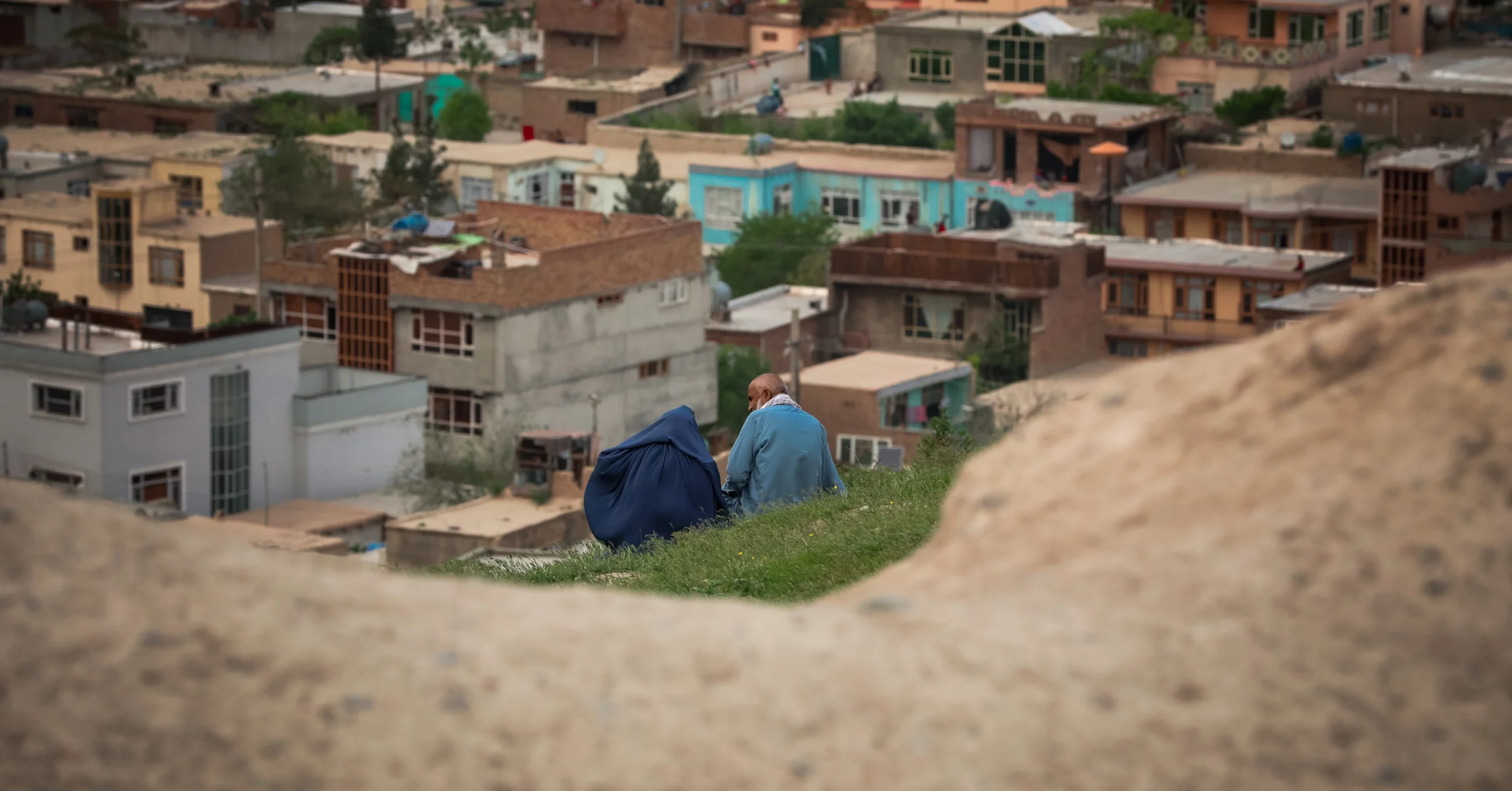 Afghan man and woman seated on a hill over a village.
