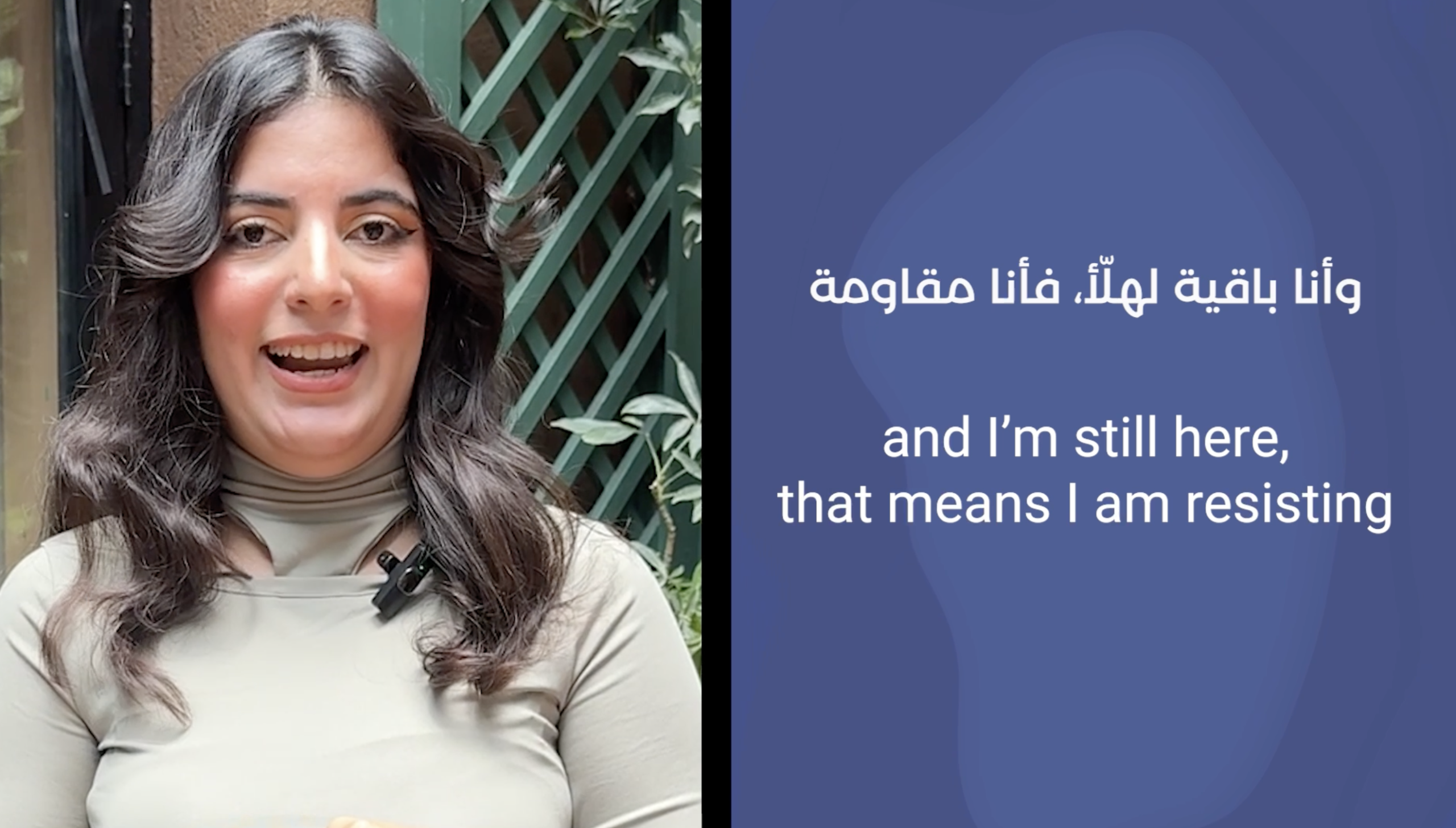 A woman with long dark hair is speaking outdoors, wearing a beige top and a microphone. Next to her, text in Arabic and English reads: and I’m still here, that means I am resisting.