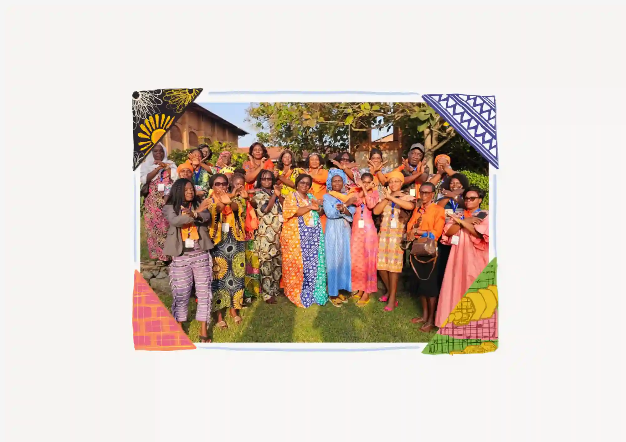 A group of women in colourful, patterned clothing stand closely together outdoors, smiling and posing for the camera. The photo is framed by vibrant geometric designs in the corners.