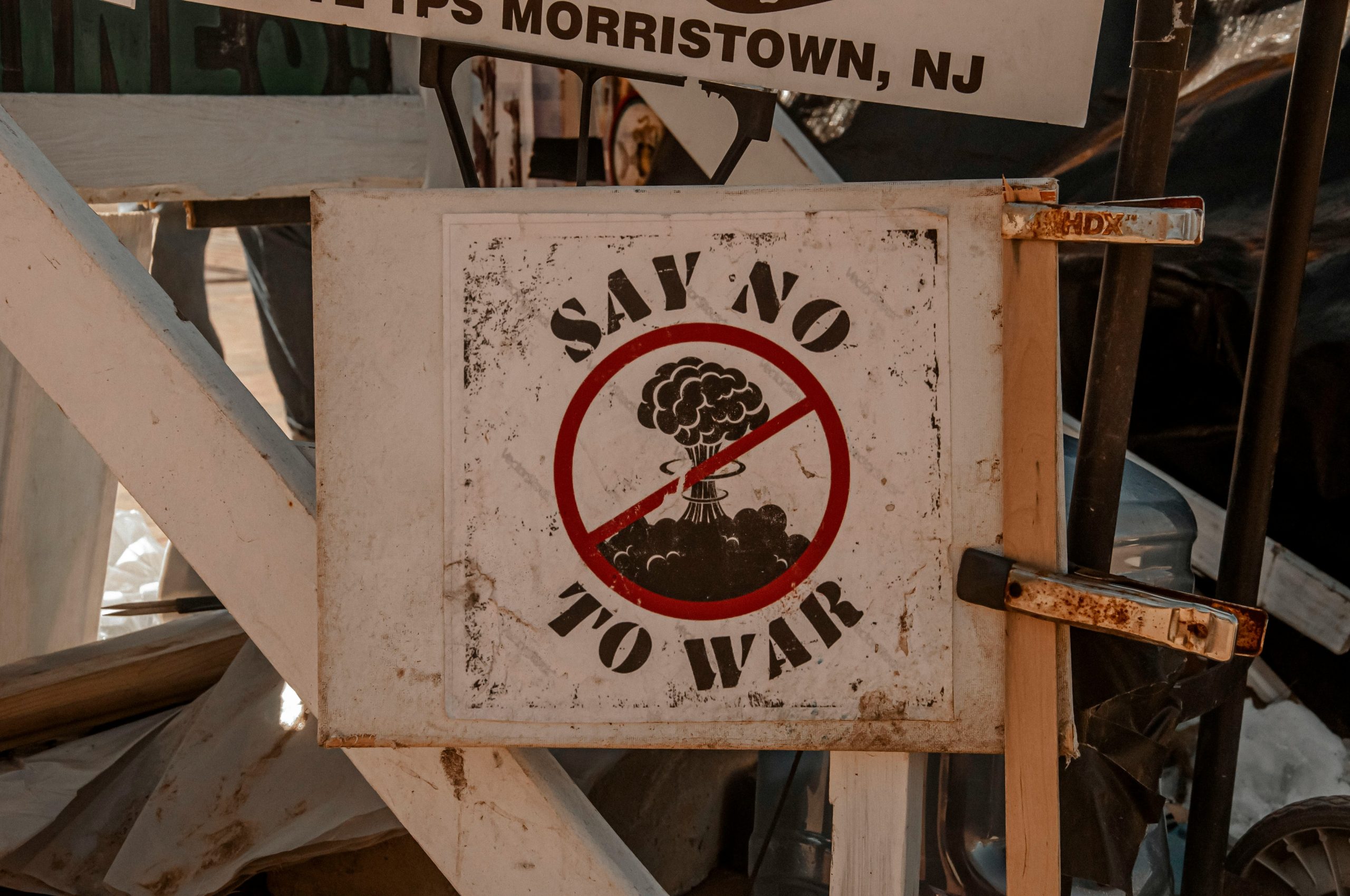 A sign with an image of a nuclear explosion inside a red prohibition circle, with the words “Say No To War” written around it, is attached to a wooden structure.